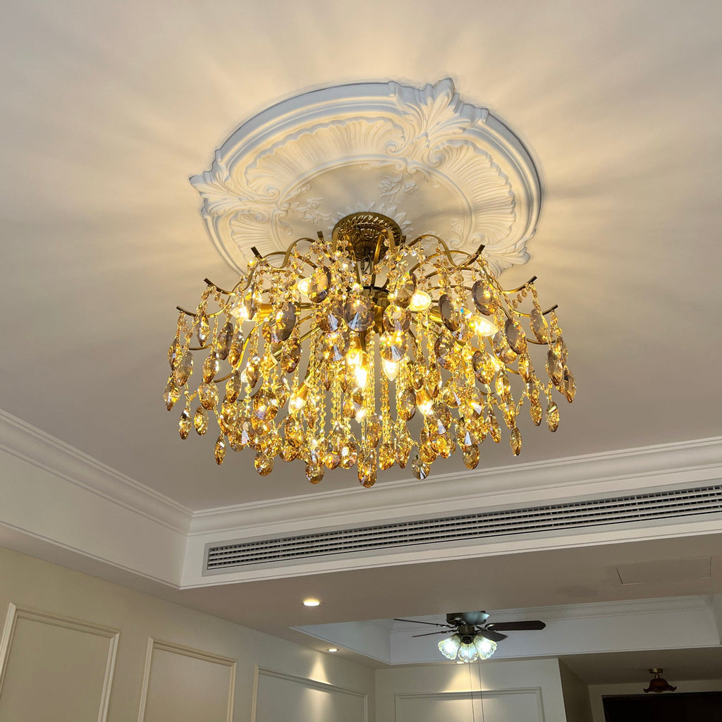 Amber crystal chandelier from Clérachic lit under a decorative white ceiling rose, with an air-conditioning vent along the cornice behind.