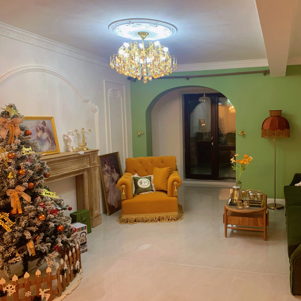 Living room with a green wall, a mustard armchair and a Christmas tree, with a Clérachic chandelier lit under a ceiling rose.