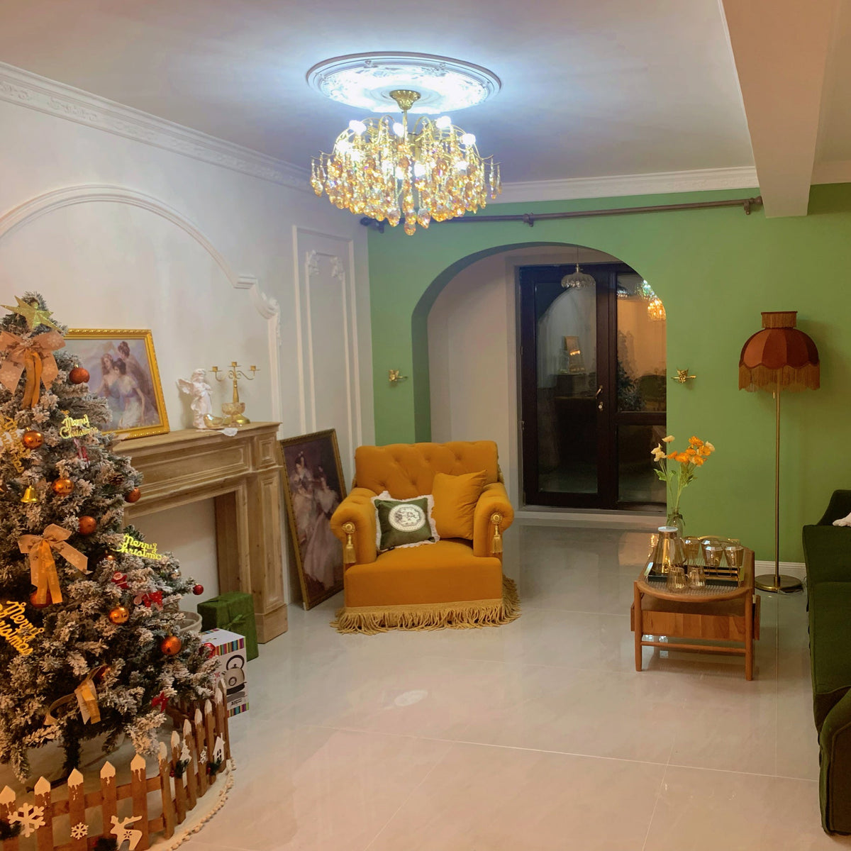 Living room with a green wall, a mustard armchair and a Christmas tree, with a Clérachic chandelier lit under a ceiling rose.