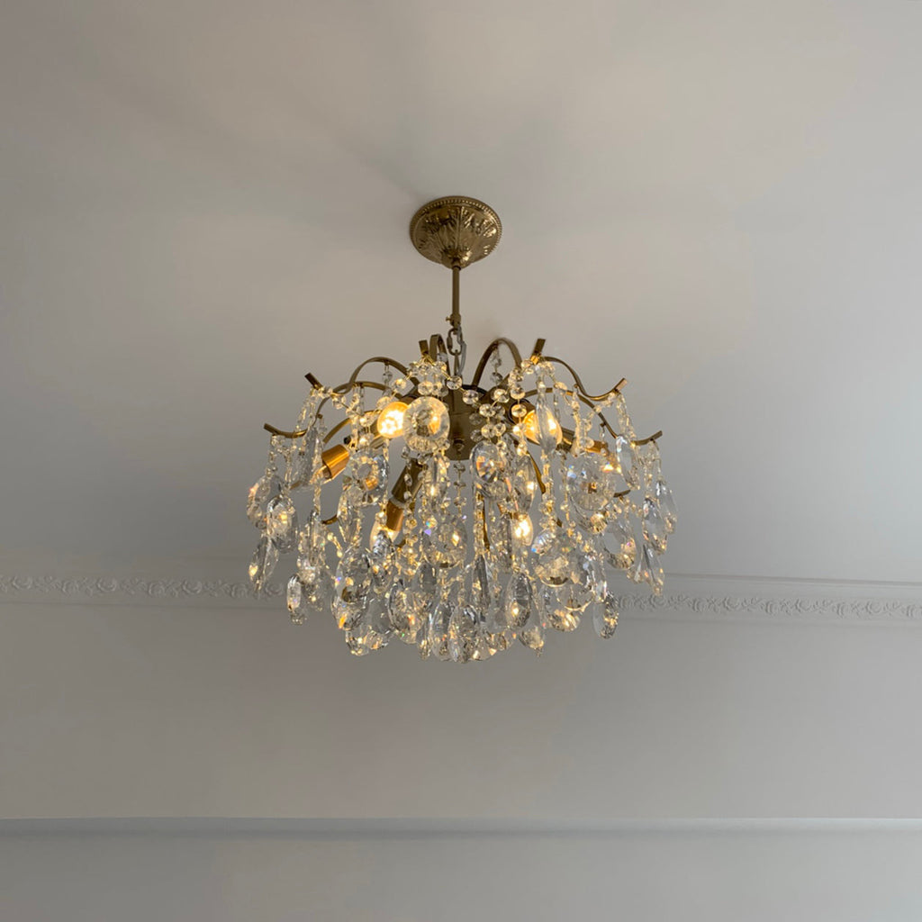 Clear crystals on a Clérachic chandelier fitted close to a pale ceiling, with a plain cornice line running behind it.