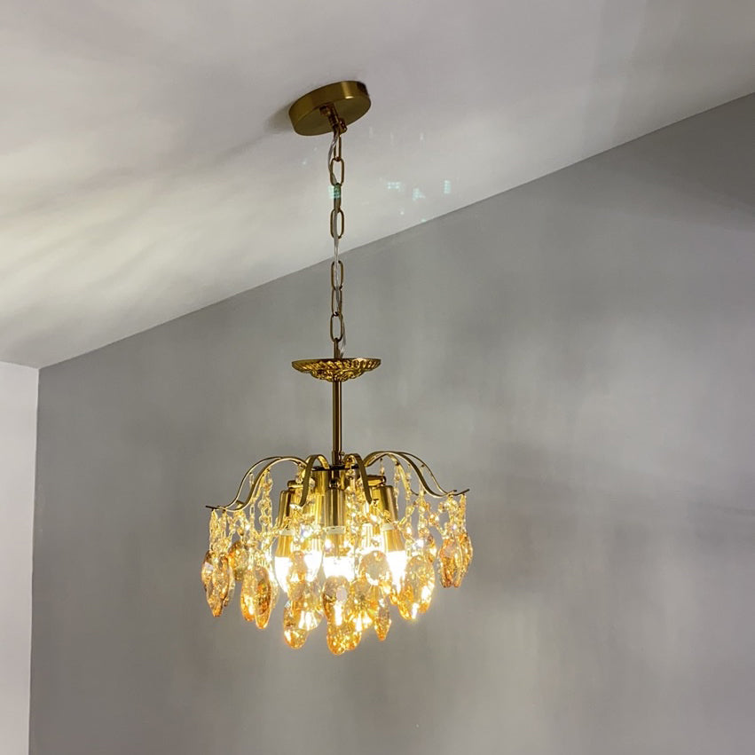 Clérachic chandelier on a chain, lit with amber crystals against a blue-grey wall and a sloping white ceiling.