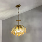 Clérachic chandelier on a chain, lit with amber crystals against a blue-grey wall and a sloping white ceiling.
