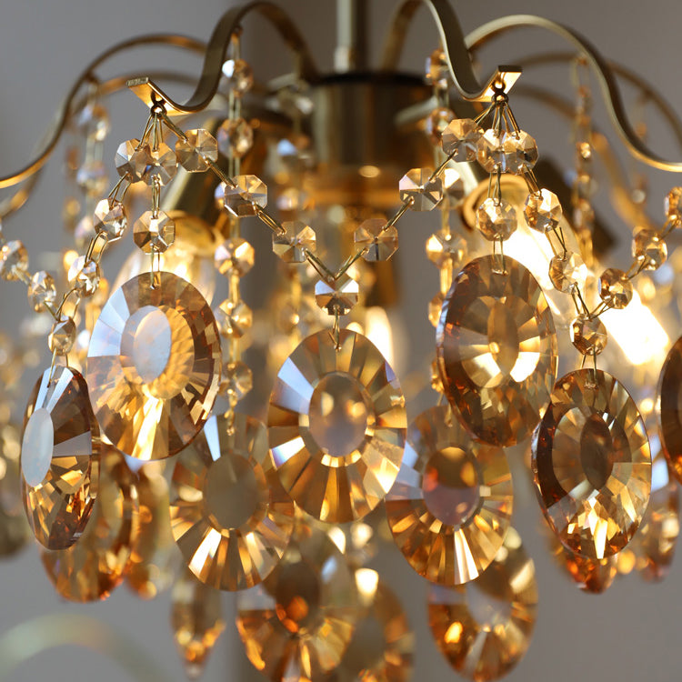Close view of round amber crystal discs strung with small beads on this Clérachic chandelier, with lit bulbs behind.