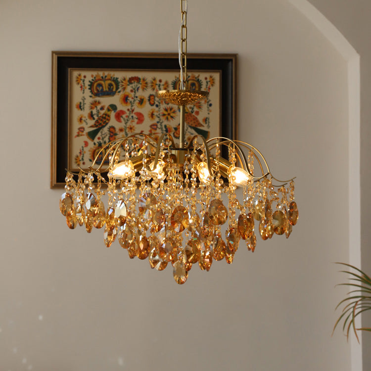 Lit Clérachic chandelier with amber crystals hung in front of a framed folk-art textile on a pale wall.