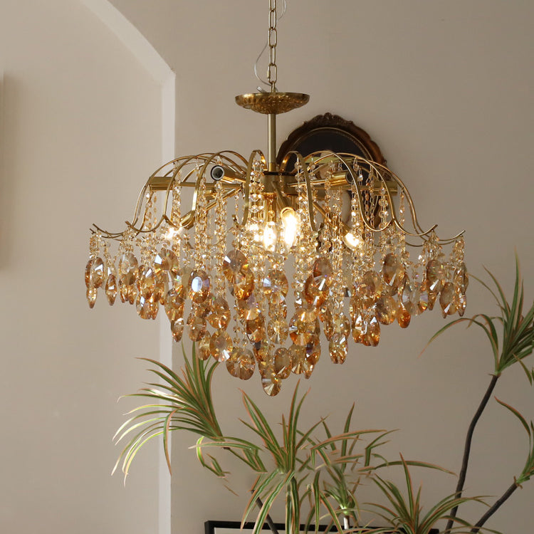 Clérachic chandelier with rich amber crystals, hung on a chain in front of a dark framed portrait and a leafy plant.