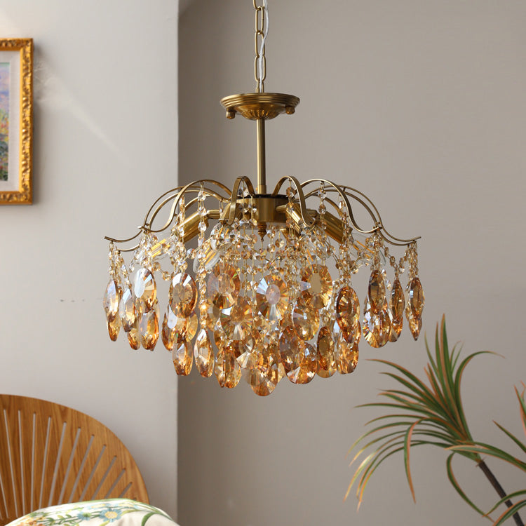 Full amber crystal drops on this Clérachic chandelier, hung beside a gilt frame with a woven chair back at the lower edge.