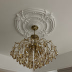View from below of this Clérachic chandelier under an ornate white ceiling rose, its crystals and brass arms catching the light.