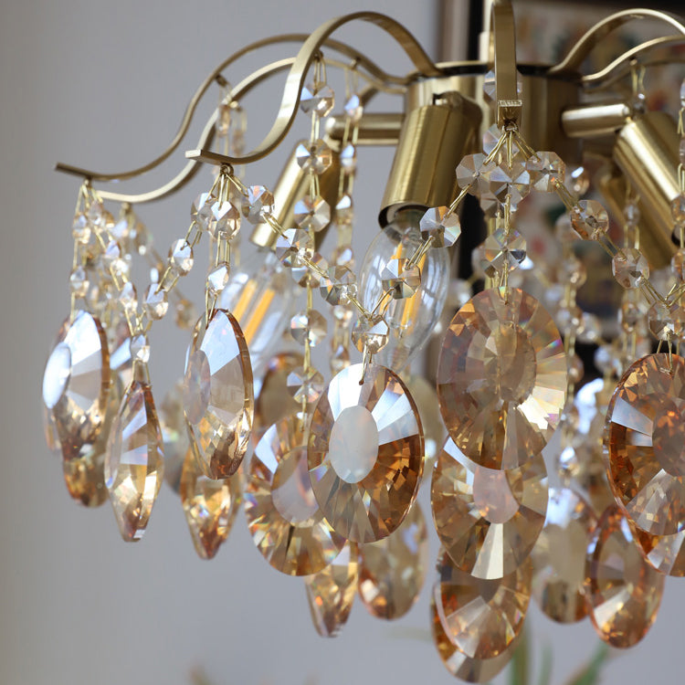 Close view of the amber crystal drops, brass candle-style sockets and curved arms on this Clérachic chandelier.