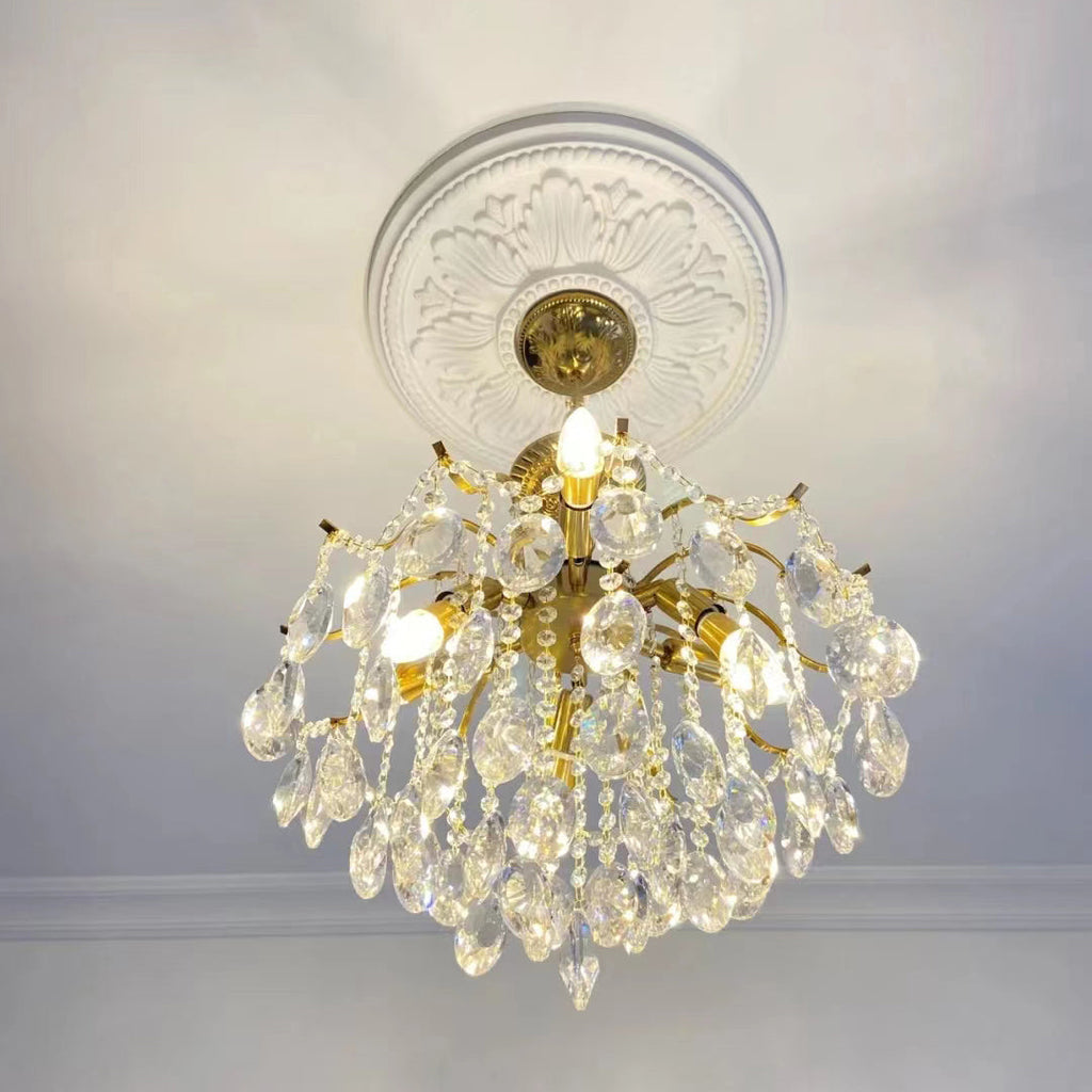 Clear crystal Clérachic chandelier with lit candle-style bulbs, hung under a white ceiling rose above a plain cornice.