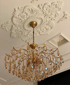 View from below of a Clérachic chandelier with amber crystals, under a detailed white plaster ceiling rose beside a recessed panel.