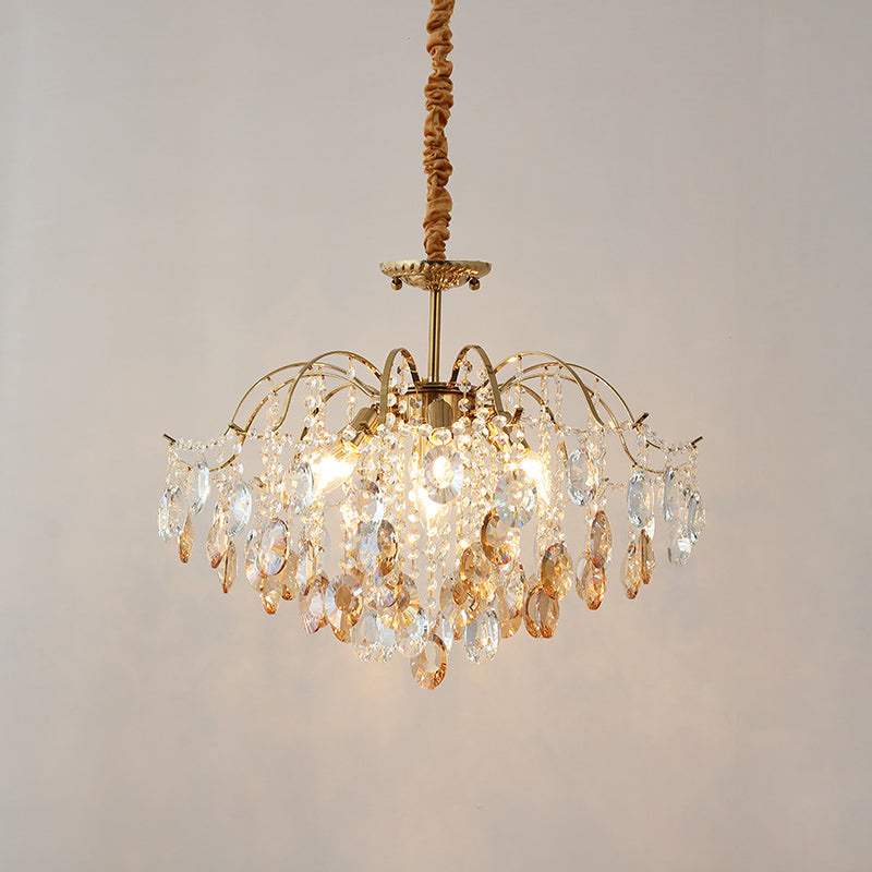Lit Clérachic chandelier with amber and clear crystals, hung from a fabric-wrapped cord against a soft grey backdrop.
