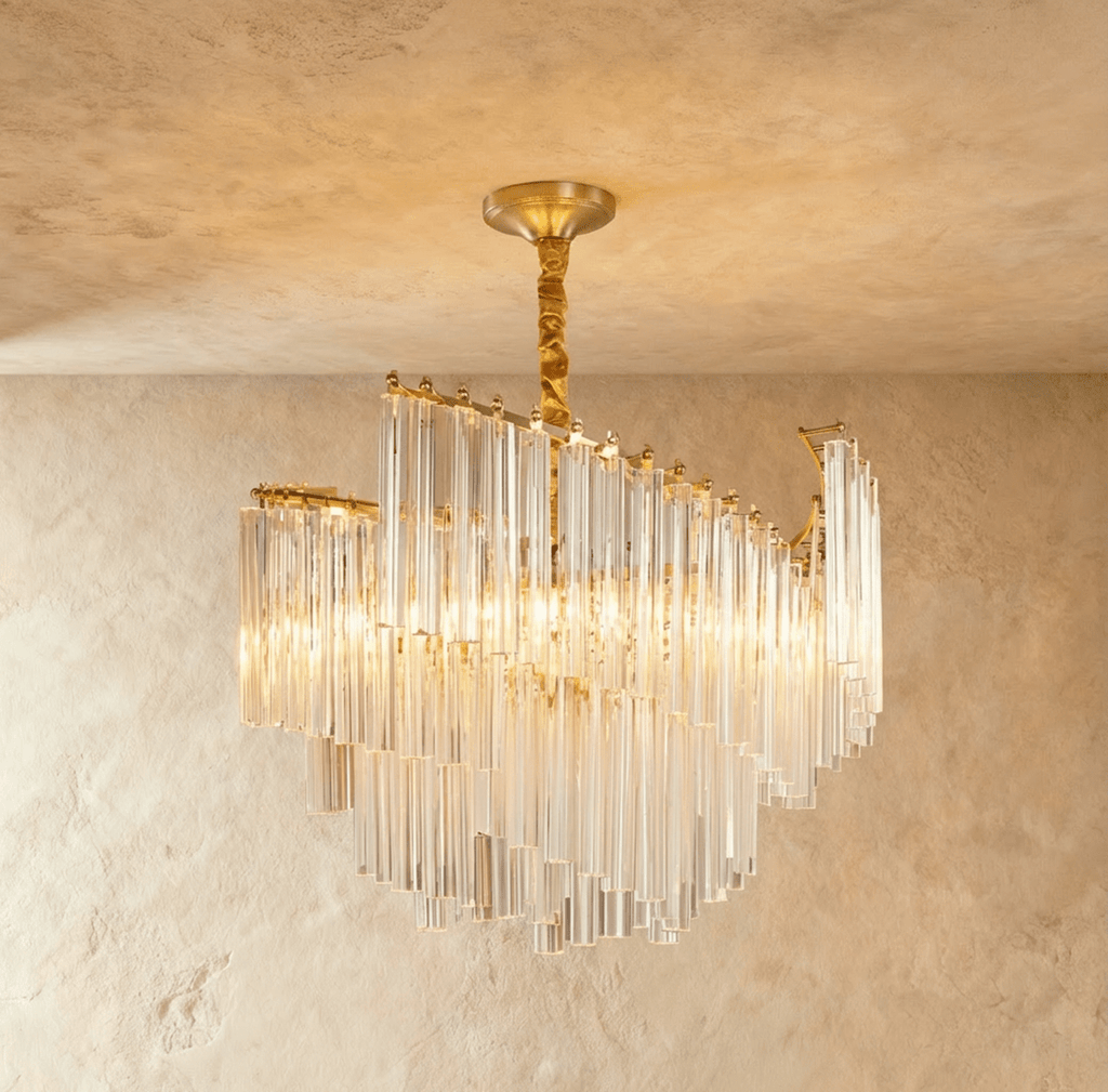 Clérachic tiered chandelier of clear crystal rods on a brass-toned frame and twisted stem, glowing warm against limewash.