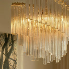 Clérachic close-up of fluted clear glass rods cascading in staggered lengths, lit from within by warm bulbs.