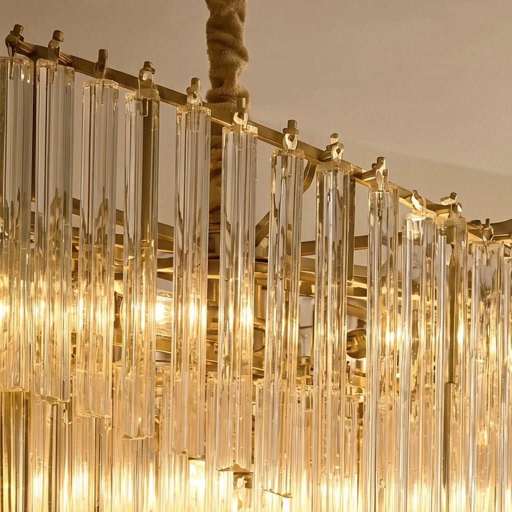 Clérachic detail of the gold-toned frame, hooks and clear crystal rods, with a wrapped chain above and bulbs glowing below.