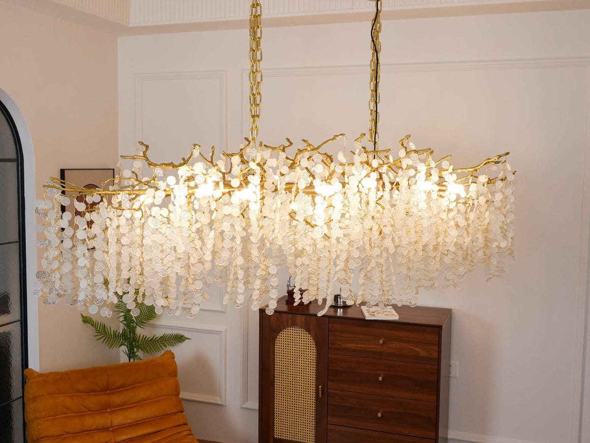 Warm light glows through the frosted crystal discs of this Clérachic chandelier, with a fern and a wooden sideboard below.