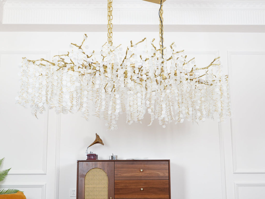 Unlit Clérachic chandelier in a white-panelled room, showing the brass branches and pale crystal discs above a walnut sideboard.