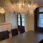 Lit Clérachic chandelier seen from below in a dining room, above a dark table, with navy chairs and a tall arched door.