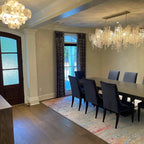 Clérachic chandelier hung in a dining room with a patterned rug, navy velvet chairs and tall windows with dark curtains.
