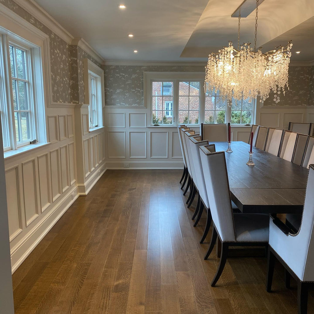 A Clérachic chandelier at the far end of a long, panelled dining room, with a dark table and pale chairs in the foreground.