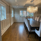 A Clérachic chandelier at the far end of a long, panelled dining room, with a dark table and pale chairs in the foreground.
