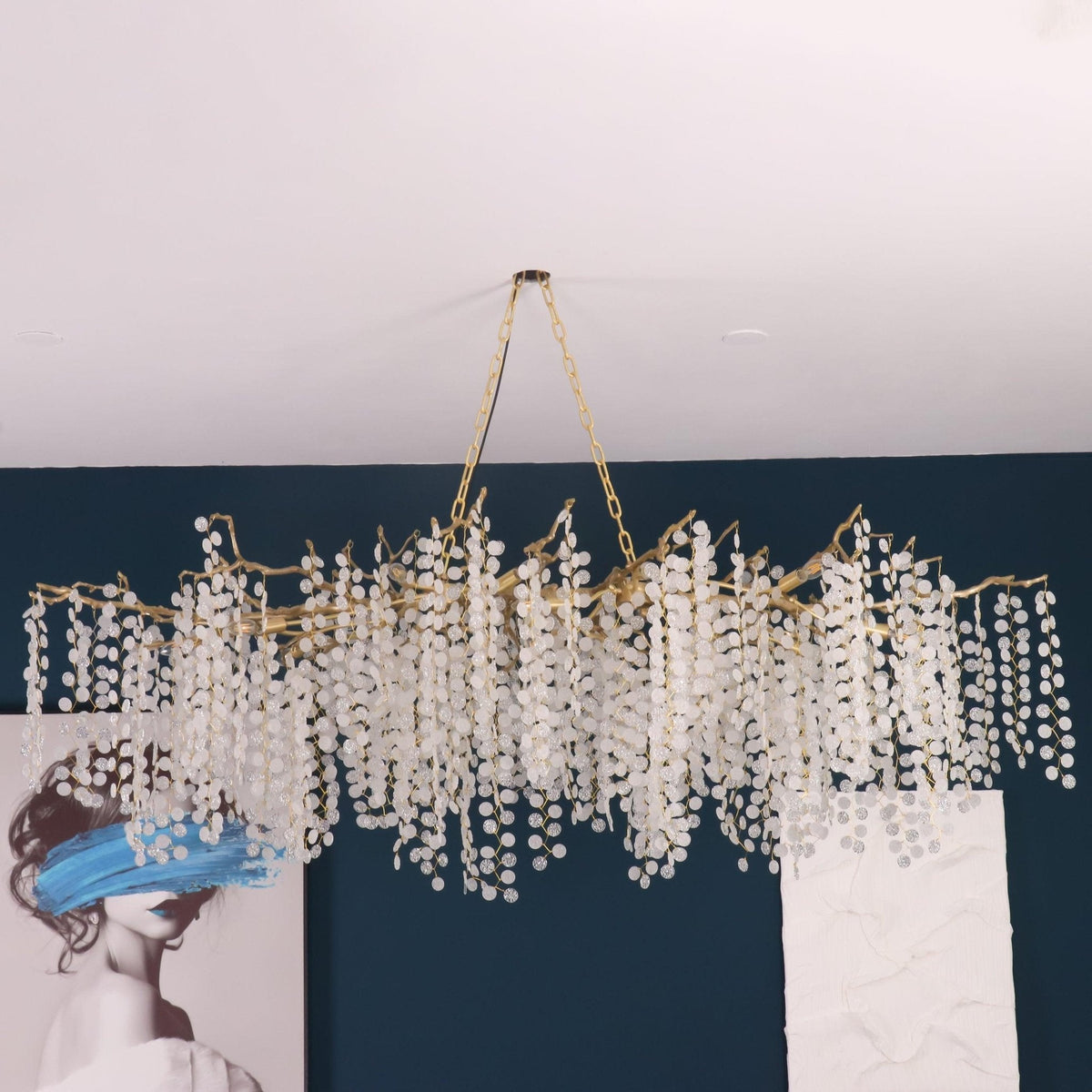 Looking up at a Clérachic chandelier hung from two chains in a room with a teal wall and a white ceiling.