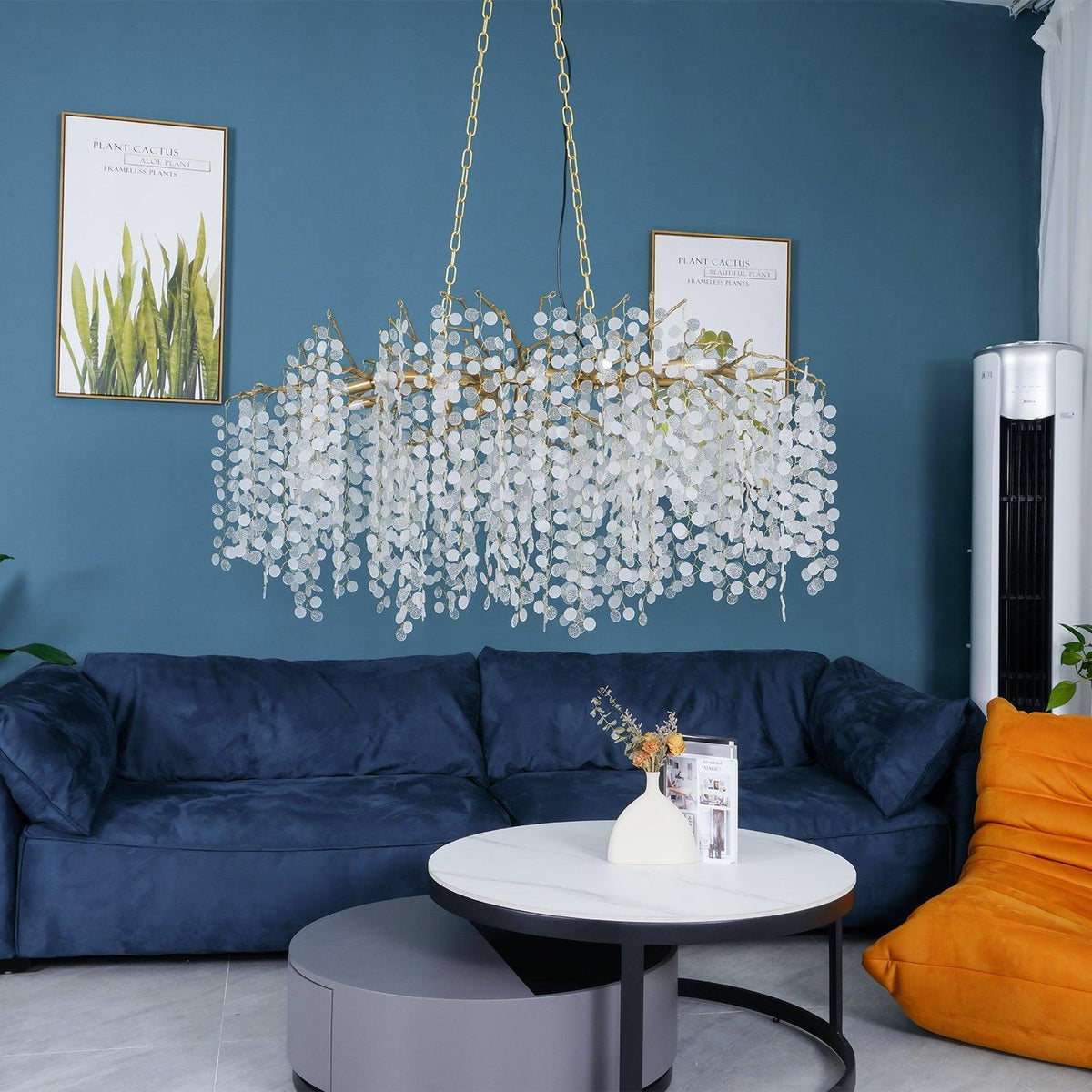 Clérachic chandelier hung above a navy velvet sofa and round white coffee tables, with a teal wall and an orange bean-bag chair.