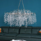 Clérachic chandelier with silver-toned branches over a green leather sofa, against a bright teal wall.