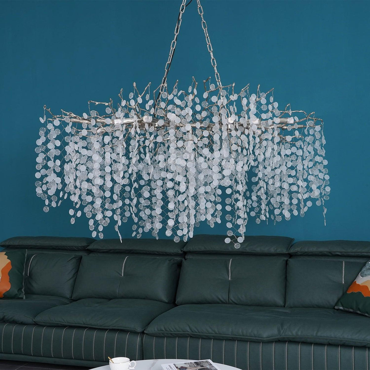 Clérachic chandelier with silver-toned branches over a green leather sofa, against a bright teal wall.