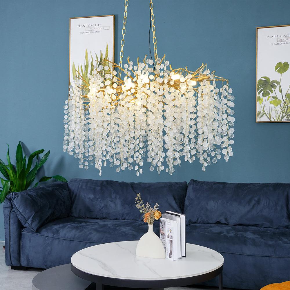Clérachic chandelier lit against a blue wall with framed plant prints, above a navy sofa and a white round table.