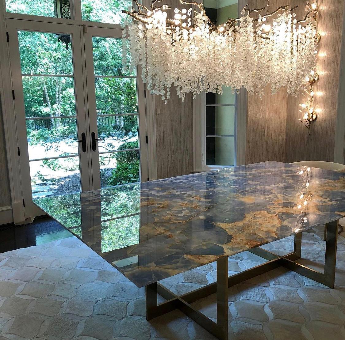 Clérachic chandelier hung over a glossy blue and gold stone table, with garden doors and a wall light at the side.