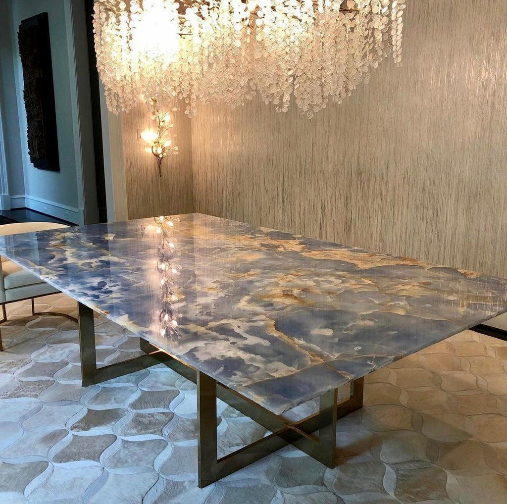 The Clérachic chandelier above a blue and gold stone table on brass legs, with a textured wall and a wall light behind.