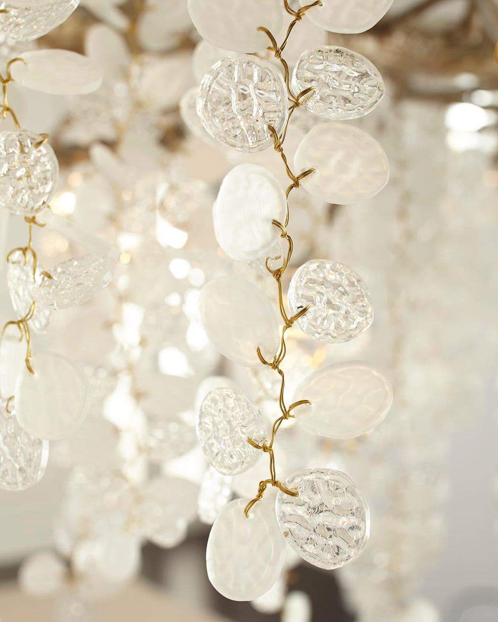 Close view of the frosted and textured glass discs on this Clérachic chandelier, strung along a slim brass branch.