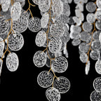 Close view of clear, hammered-texture glass discs on thin brass branches, part of this Clérachic chandelier, on black.