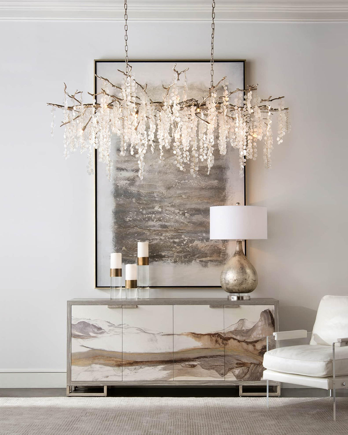 Clérachic chandelier hung over a white sideboard with a landscape pattern, with a framed abstract painting and a table lamp.