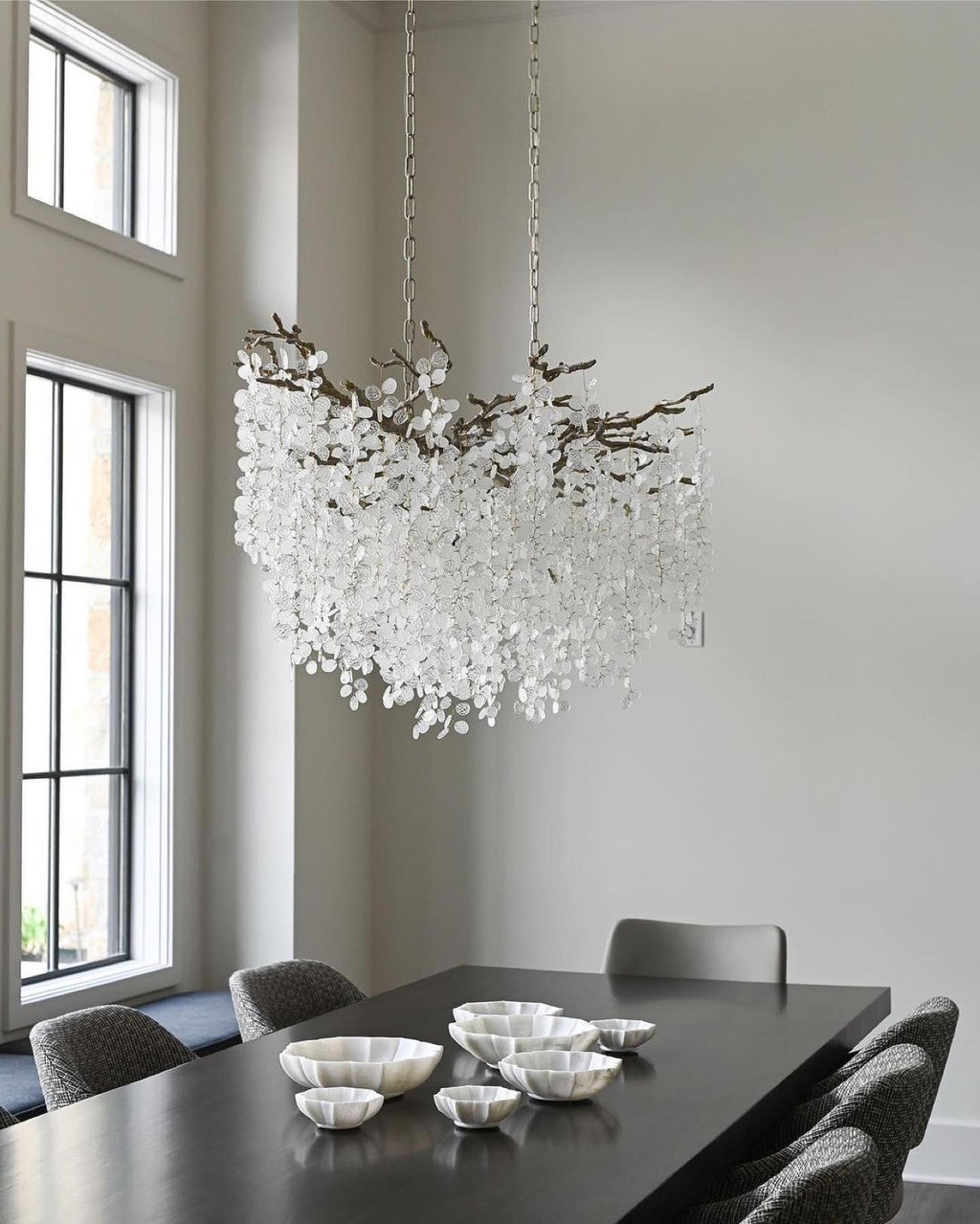Looking up at the Clérachic chandelier in a bright room with tall windows, with a dark table and small silver bowls below.