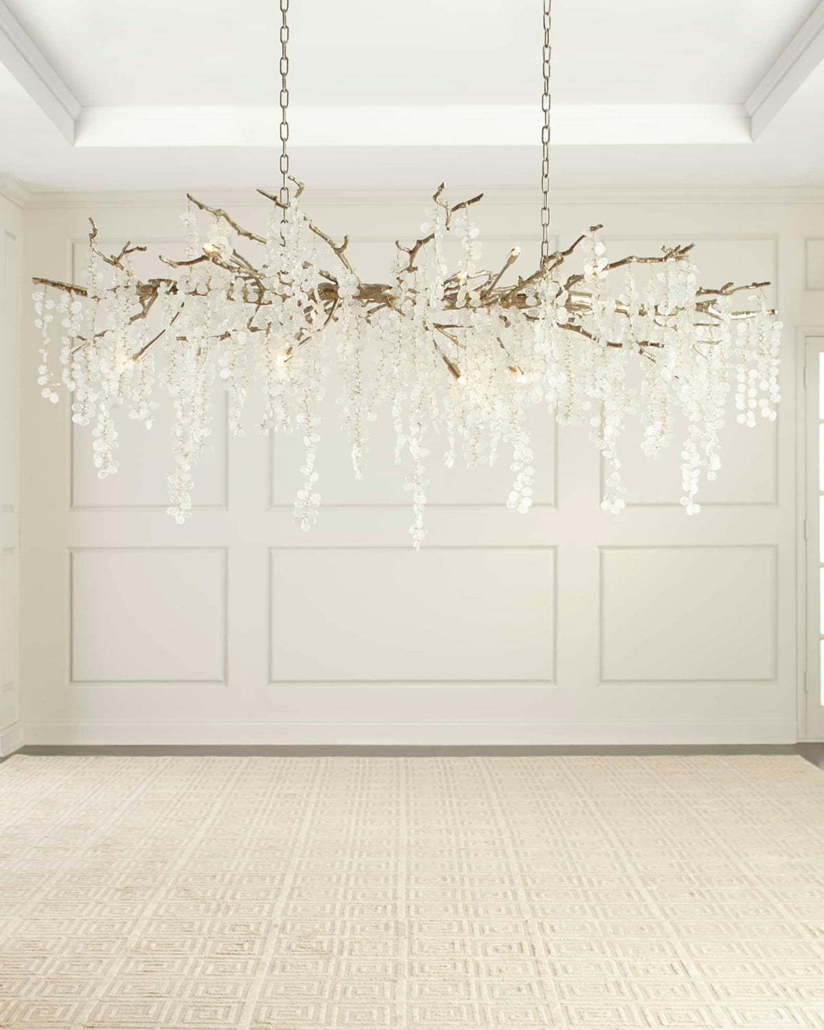 Clérachic chandelier hung in an empty, white-panelled room with a pale rug, shown evenly lit from within.