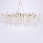 Clérachic brass branch chandelier on a soft lilac-grey backdrop, hung from a chain with crystal discs falling in straight strands.