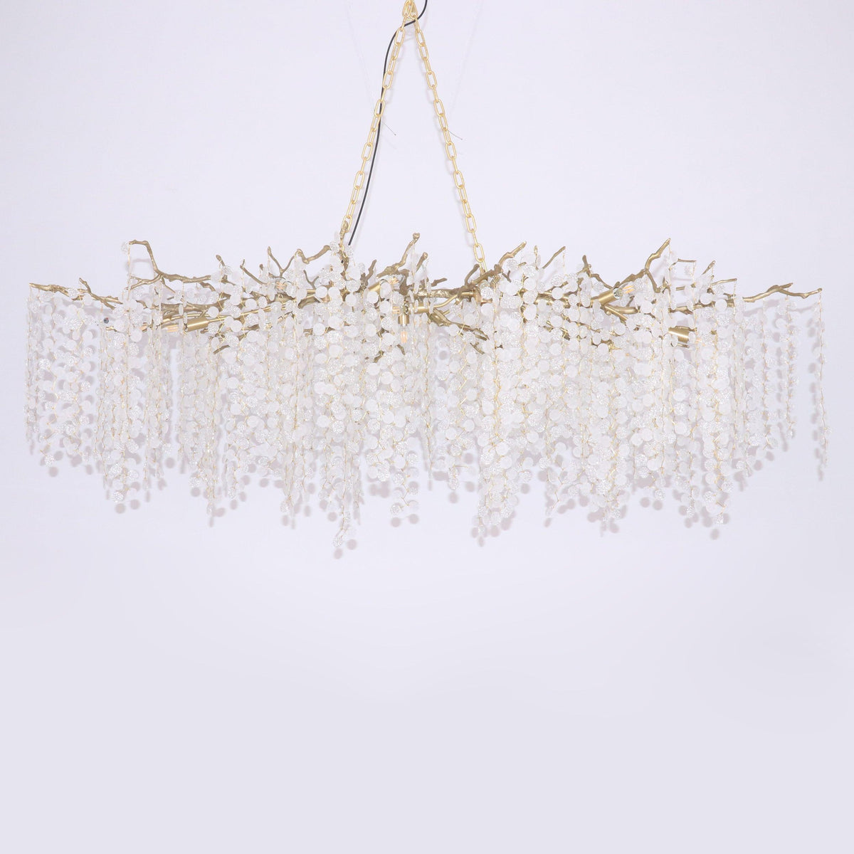 Clérachic brass branch chandelier on a soft lilac-grey backdrop, hung from a chain with crystal discs falling in straight strands.