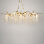 Lit Clérachic chandelier on a warm grey backdrop, with brass branches, glowing bulbs and long strands of crystal discs.