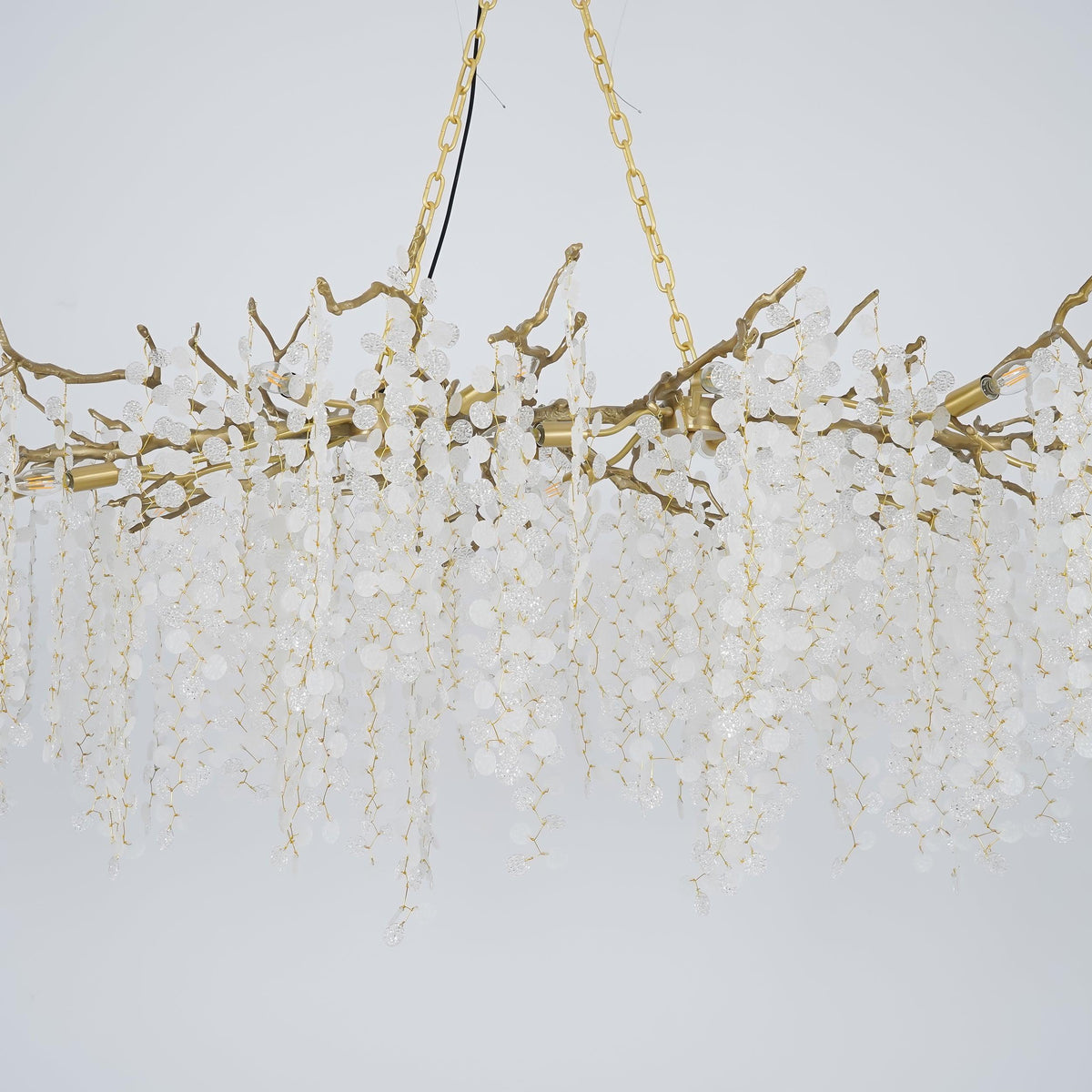 Close view of the brass branches and chain on this Clérachic chandelier, with frosted crystal strands on a pale blue-grey backdrop.