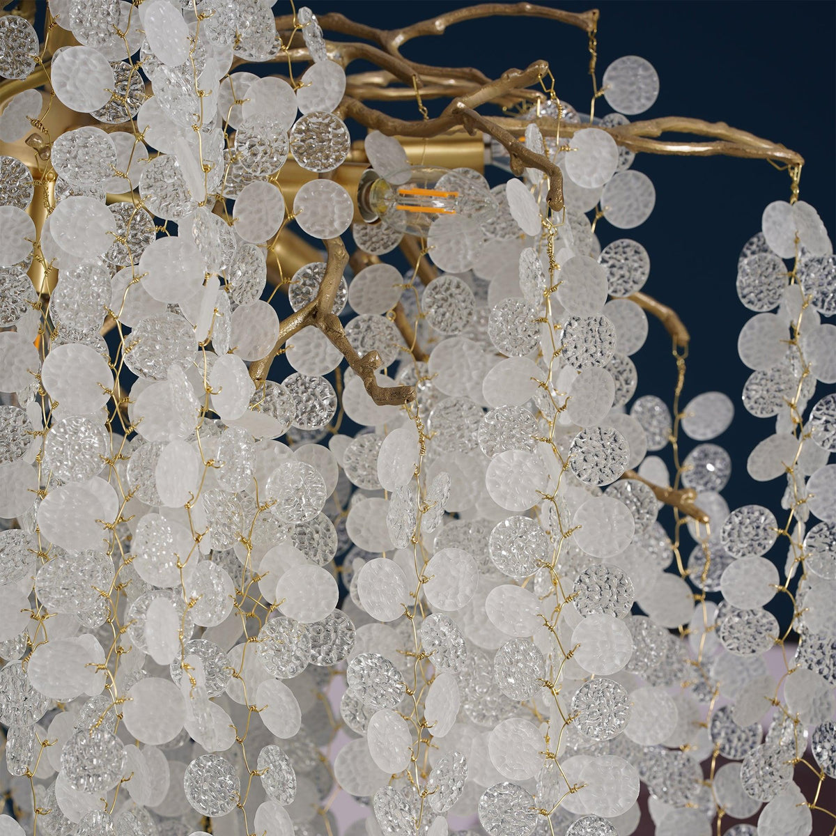 Close view of frosted and textured crystal discs on gold wire, with brass branches, from this Clérachic chandelier.