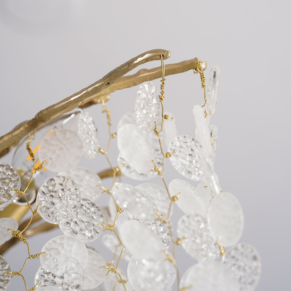Close view of a brass branch with textured glass discs tied on with fine gold wire, from this Clérachic chandelier.
