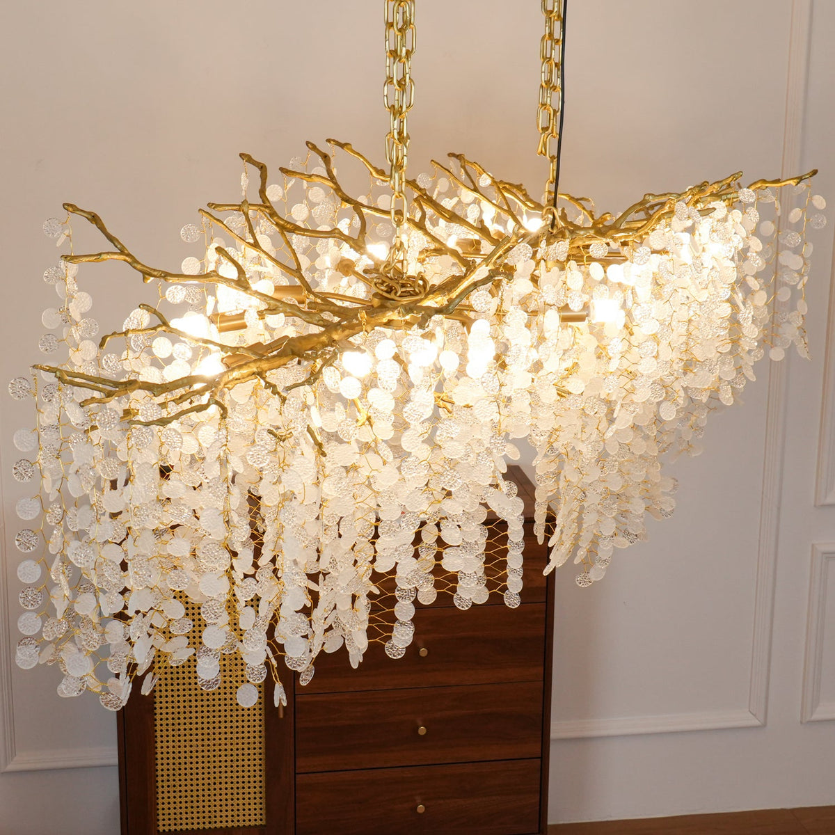 Close view of the lit Clérachic chandelier, its brass branches dense over layers of crystal strands, above a walnut cabinet.