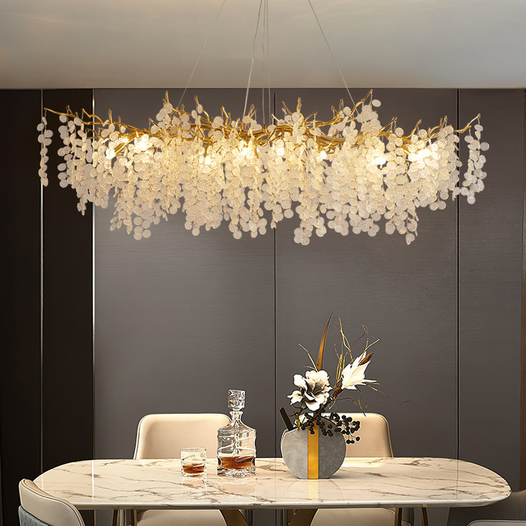 Lit Clérachic chandelier over a marble dining table, against a dark panelled wall with a decanter and a vase of flowers.