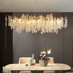 Lit Clérachic chandelier over a marble dining table, against a dark panelled wall with a decanter and a vase of flowers.