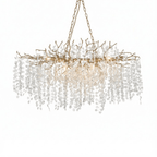 Clérachic long chandelier with brass-toned branches on a white backdrop, hung from a chain with warm bulbs glowing inside.