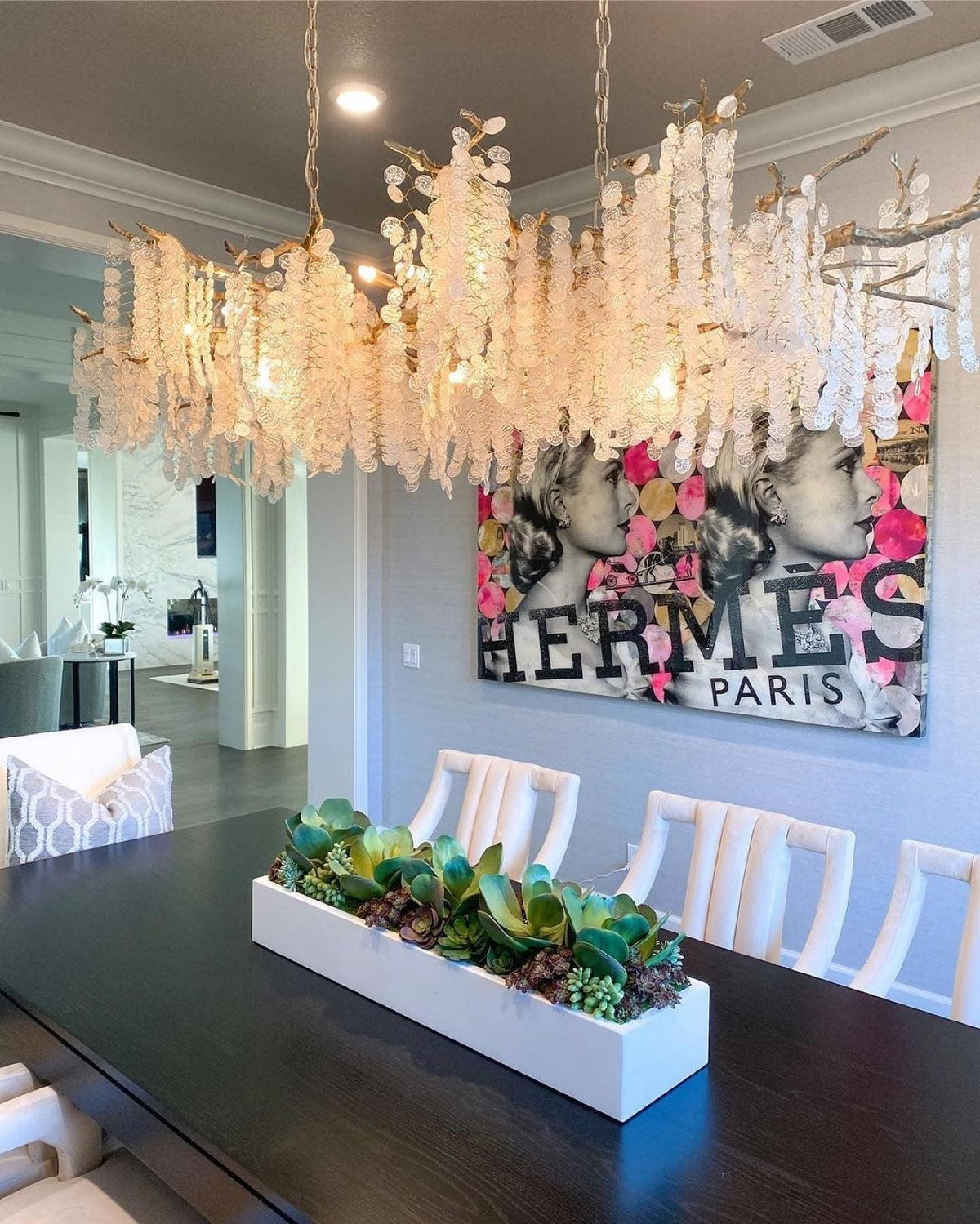 Lit Clérachic chandelier above a dark dining table in a room with a bold pink and black artwork and pale chairs.