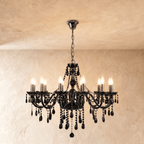Clérachic chandelier with eight black glass candle arms, lit bulbs and dense faceted crystal drops on a plaster wall.