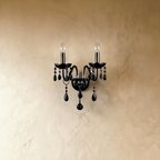 A close front view of the Clérachic wall light's black glass arms, lit candle bulbs and hanging crystal beads.