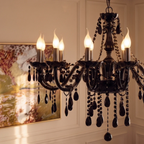 A close view of the Clérachic chandelier's lit candle arms and black glass crystal drops, a painting soft behind.